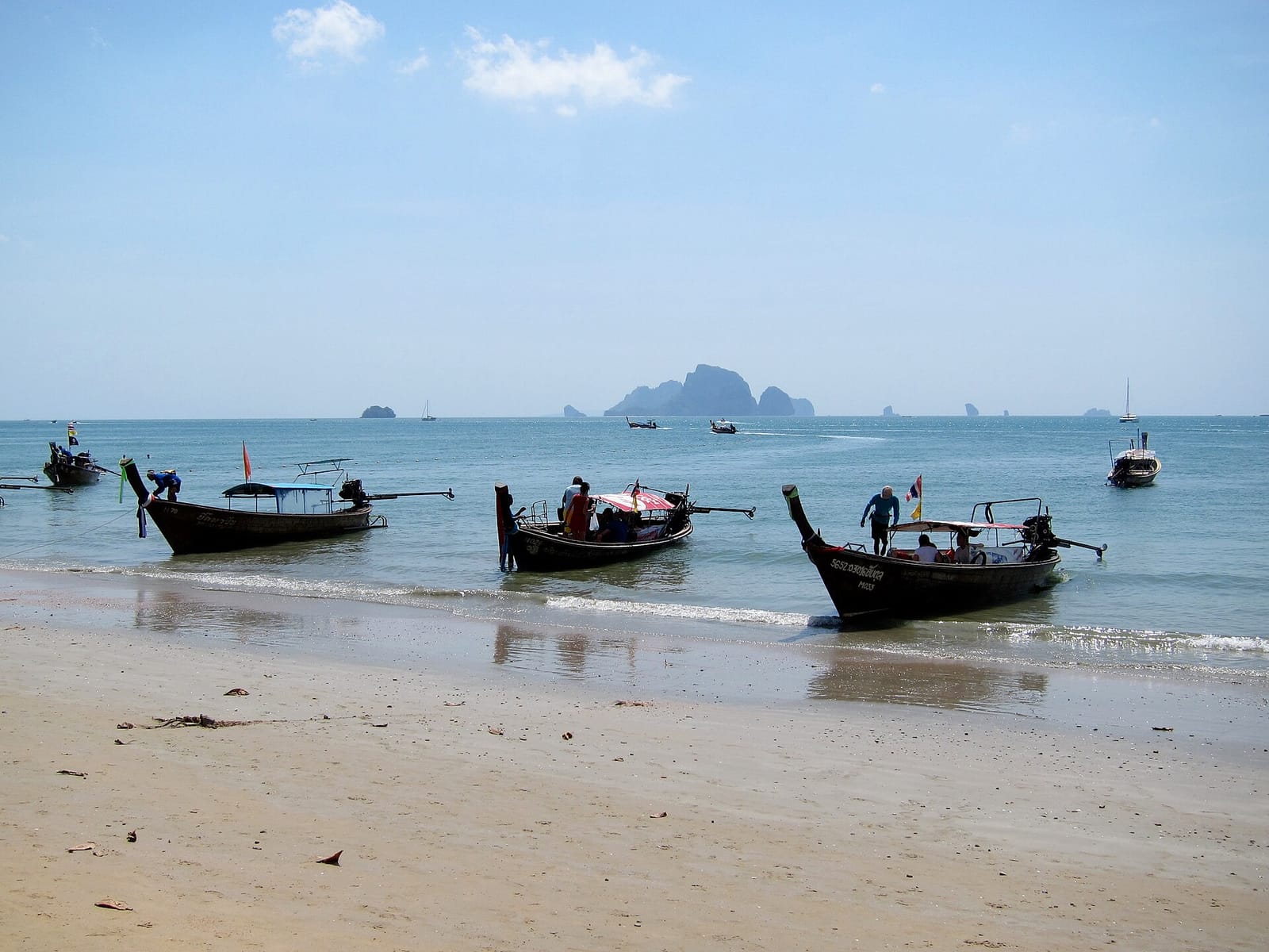 Longtail boats lined up on Ao Nang beach in Krabi, with limestone islands across the bay
