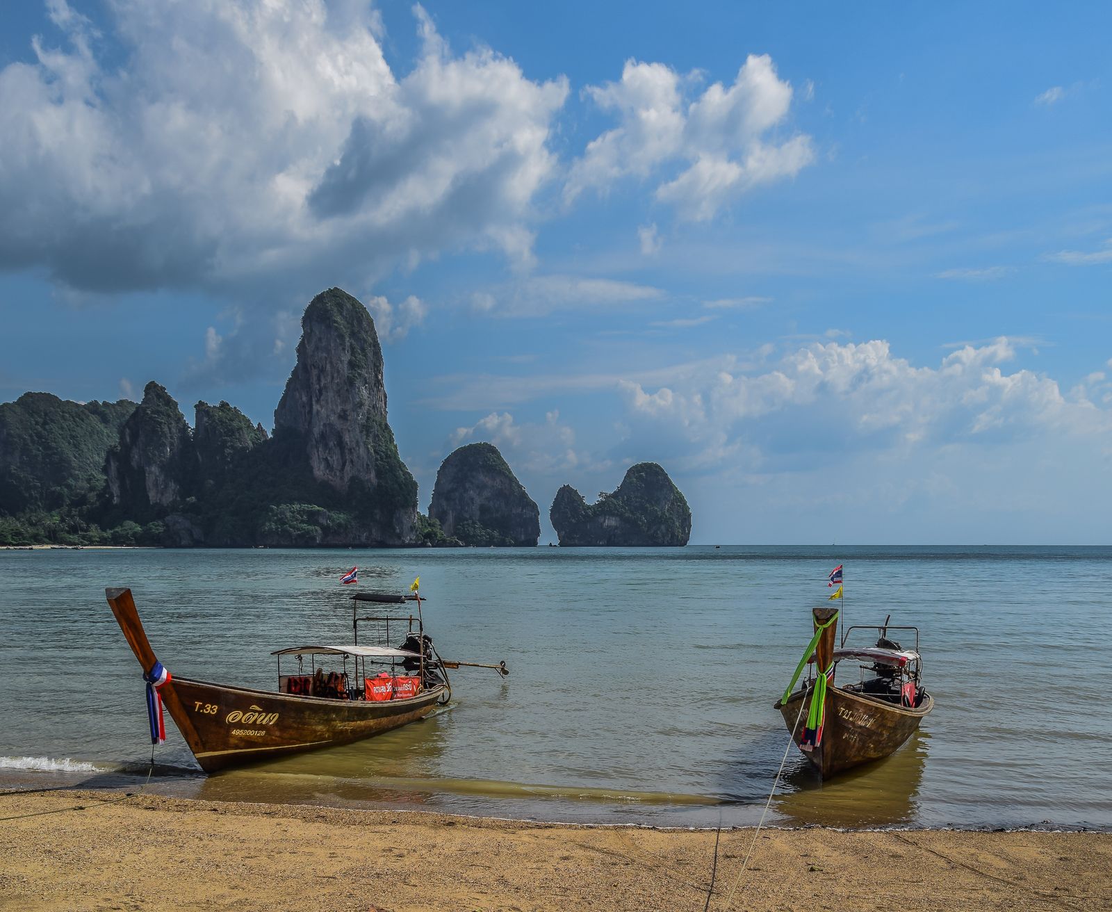 Two longtail boats on the sand at Tonsai Beach, Krabi, with limestone towers across the water