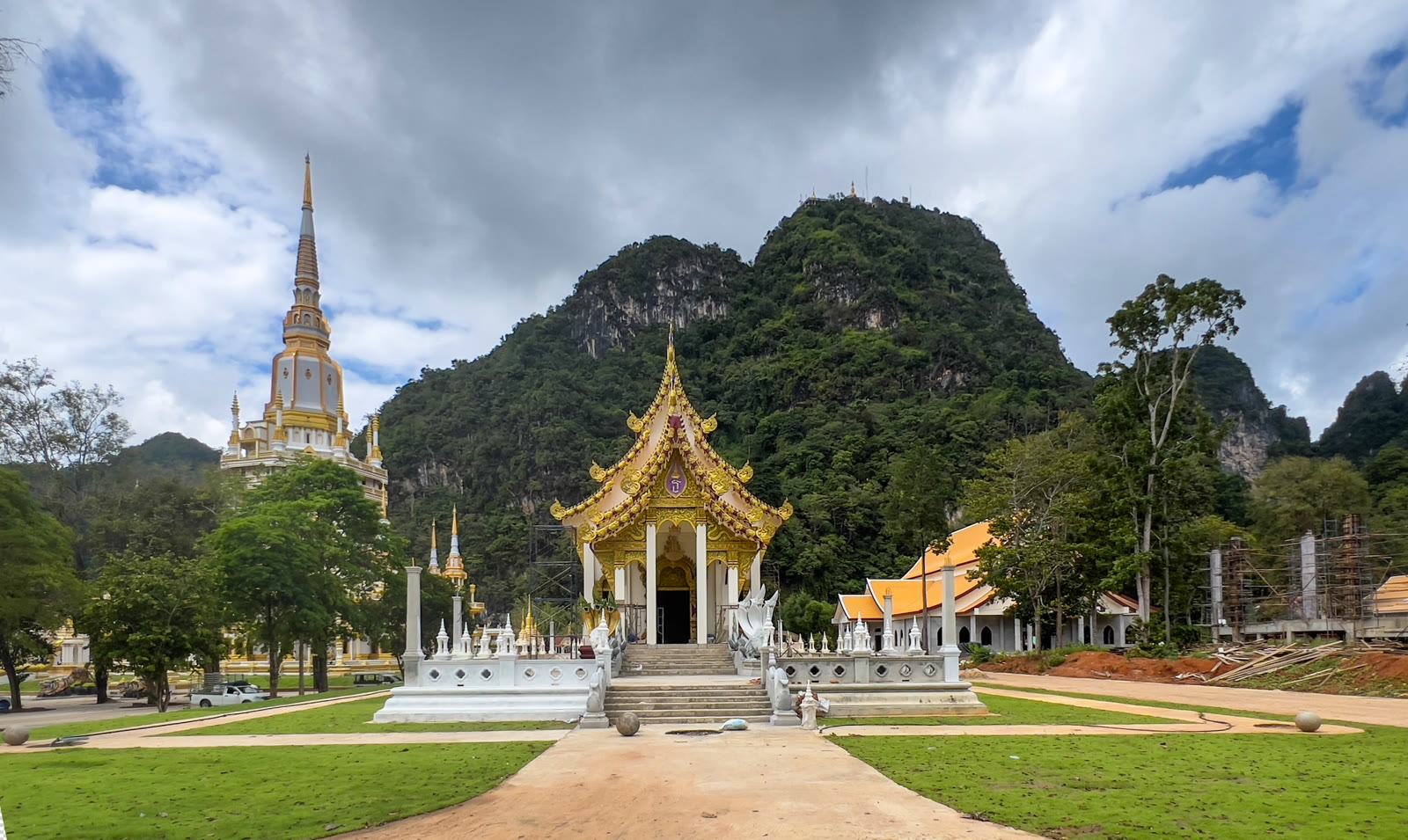 White Buddha statue on the forested hill at Wat Tham Suea, with a staircase up the slope and green valley below