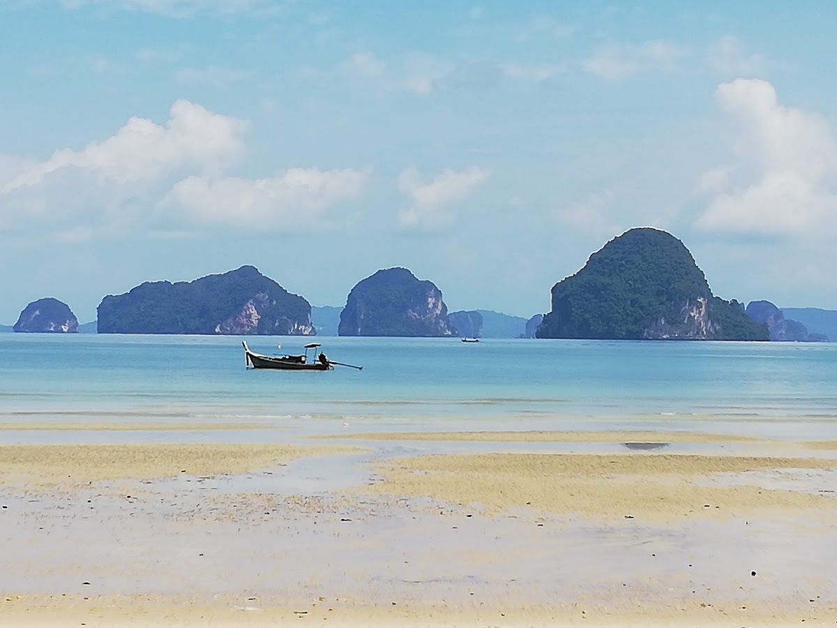 Tubkaek Beach in Krabi at low tide with a longtail boat and limestone karst islands in the distance